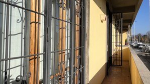 A corridor with metal bars and wooden slats, leading to a balcony with a view of parked cars and a clear sky. - Verrazzano House Florence (Firenze)
