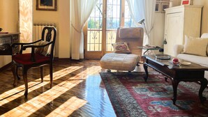 A cozy living room with a wooden floor, a red chair, a beige sofa, a small ottoman, and a glass coffee table. - Verrazzano House Florence (Firenze)
