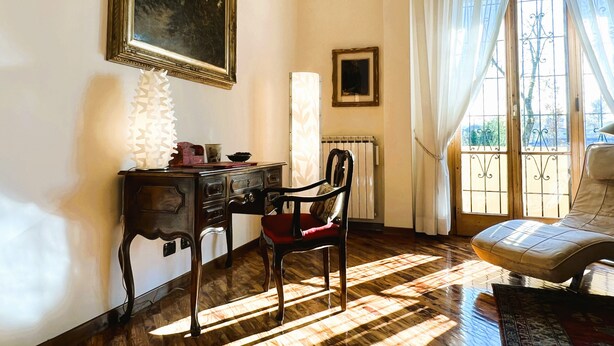A room with a wooden desk, a chair, a radiator, and a window with curtains. - Verrazzano House Florence (Firenze)