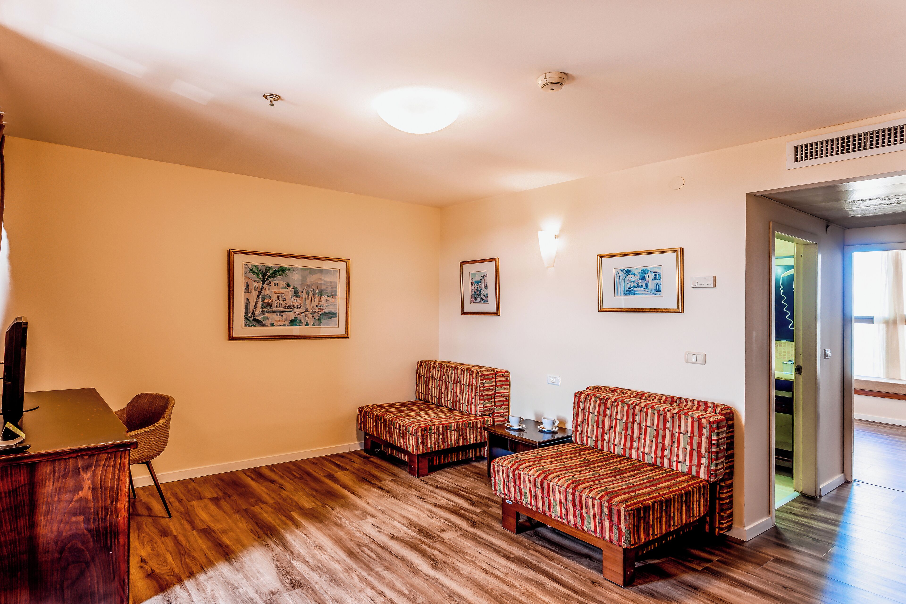 A living room with a wooden floor, two patterned sofas, a wooden coffee table, and framed pictures on the walls.