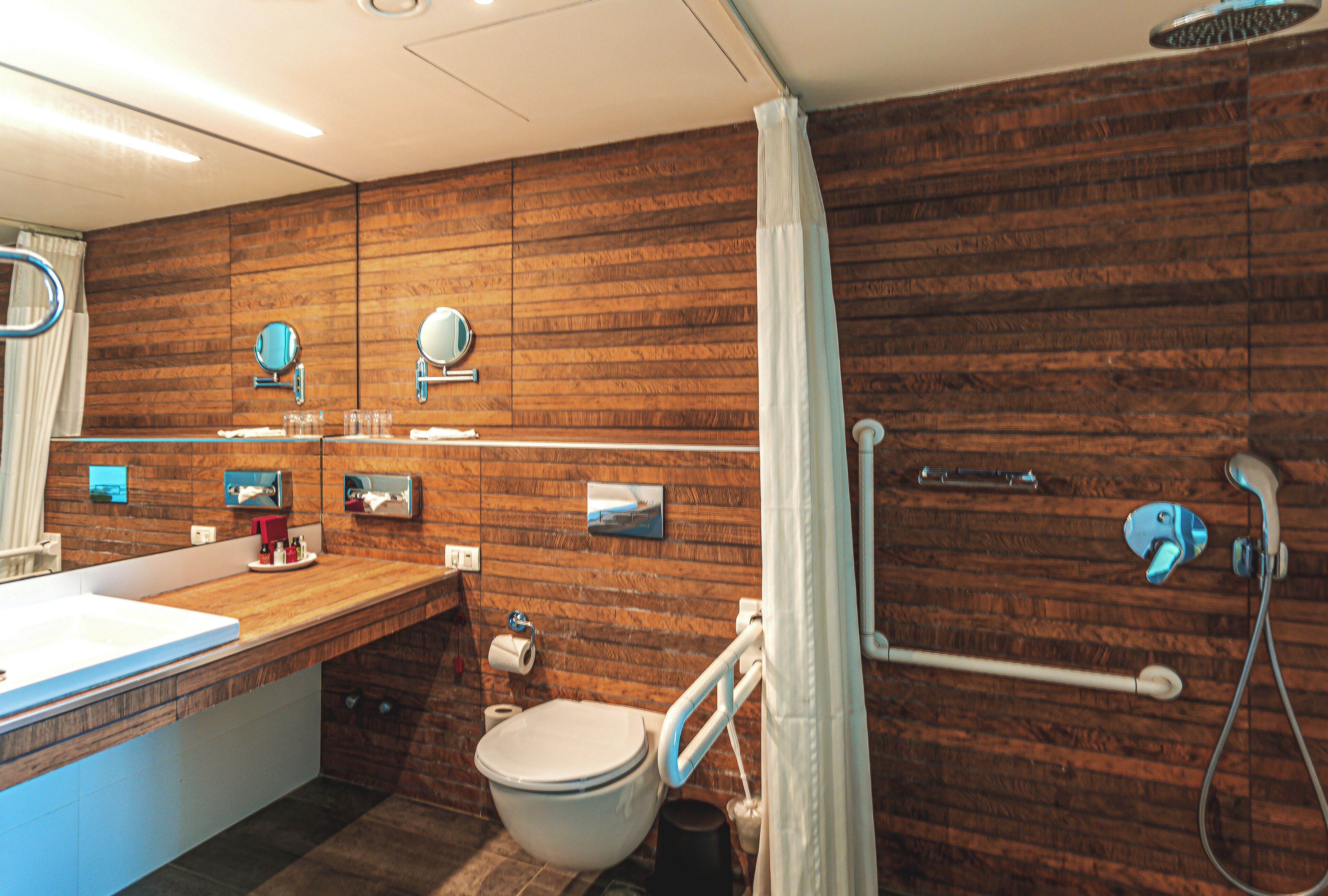 A modern bathroom with a wooden wall, a large mirror, a toilet, and a shower area.