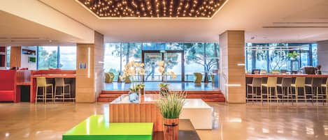 A modern lobby with a green and black seating area, a reception desk, and a large window offering a view of the outdoors.