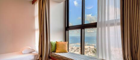 A bedroom with a bed, a window with a view of the city, and curtains.