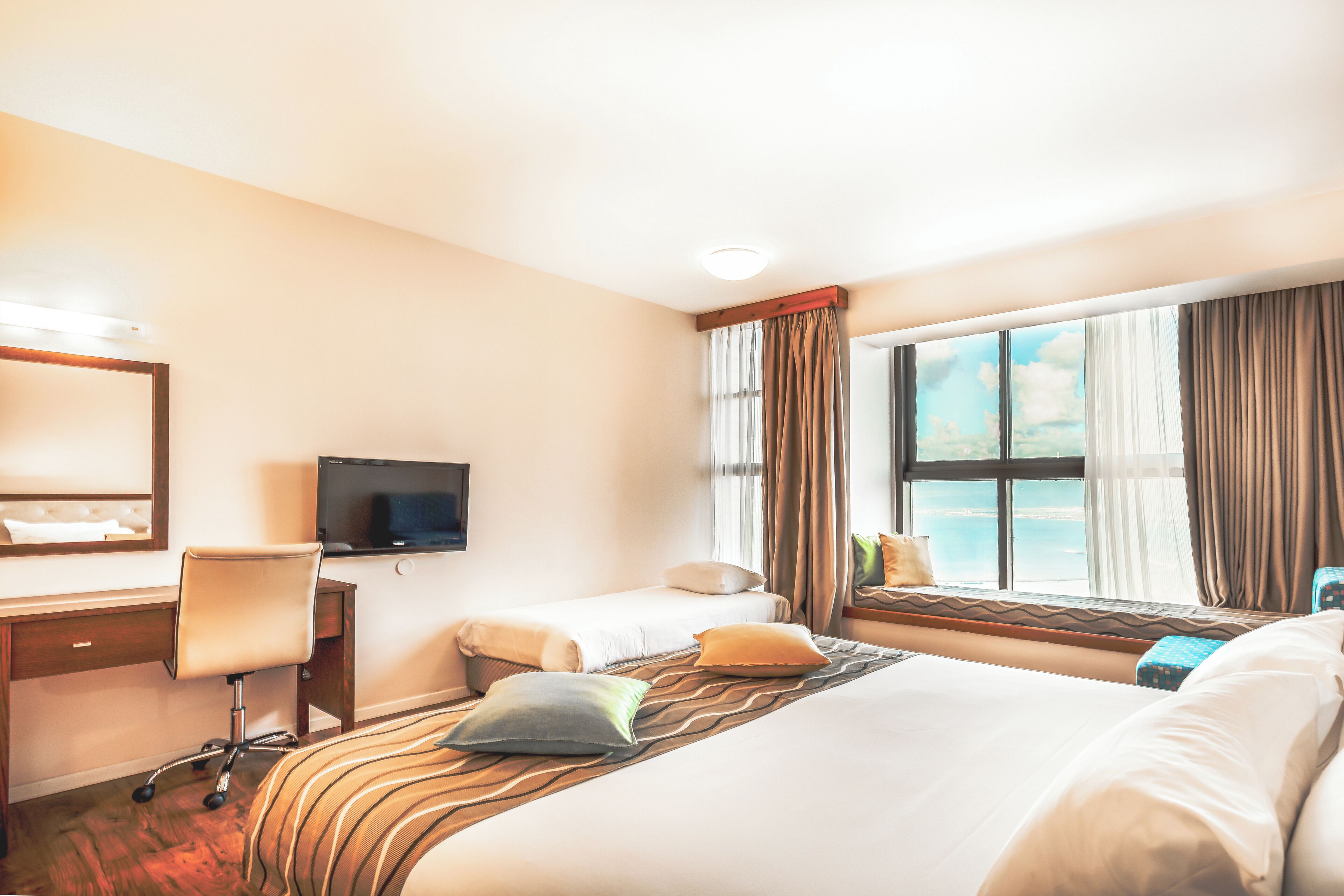 Habitación de hotel con dos camas, un escritorio, una silla, un televisor y una ventana con cortinas.