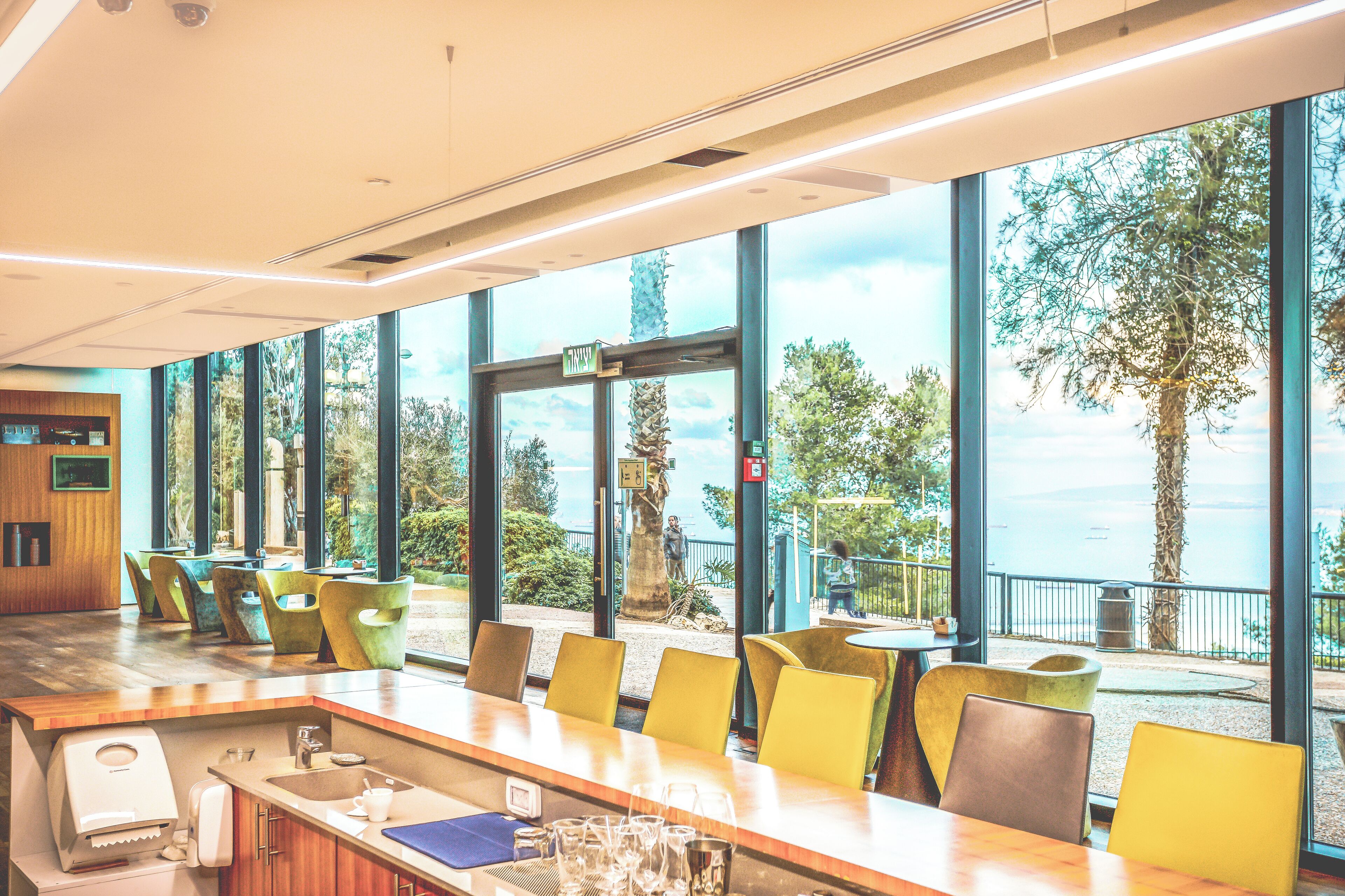 Un bar moderne avec vue sur la mer, doté d’un long comptoir, de chaises jaunes et d’un buffet en bois.