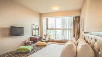 Una habitación de hotel con cama, televisión, escritorio y ventana con cortinas.