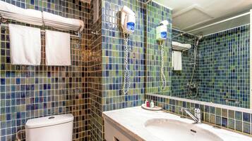 A bathroom with a tiled backsplash, a toilet, a sink with a mirror, and two hair dryers mounted on the wall.