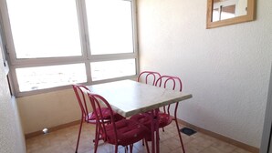 A dining area with a white table and four red chairs, a window with blinds, and a wall-mounted mirror. - Spacious apartment for 6, Valras-Plage center, 10m from the beach (Valras-Plage)