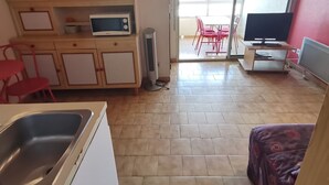 A compact living space with a kitchenette, a dining area with red chairs, a TV, and a large window. - Spacious apartment for 6, Valras-Plage center, 10m from the beach (Valras-Plage)