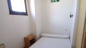 A small, clean room with a single bed, a small wooden nightstand, a radiator, and a window with a blue frame. - Spacious apartment for 6, Valras-Plage center, 10m from the beach (Valras-Plage)