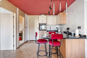 A modern kitchen with a red ceiling, wooden cabinets, and a bar area with red chairs. - Centrico 2 Hospitality - Luxury & Comfort in the Center (Tangier)