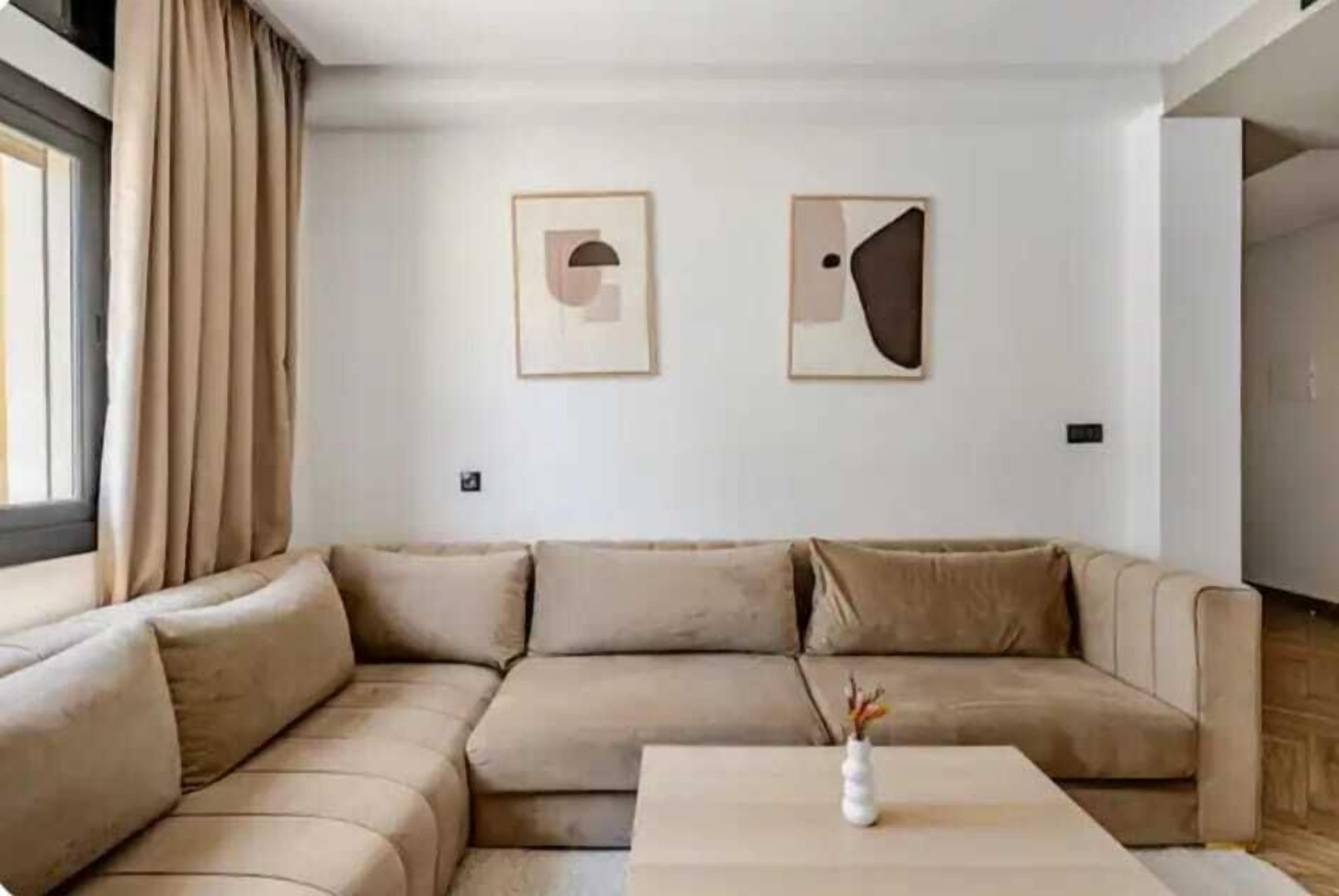 A modern living room with a beige sectional sofa, a coffee table, and two framed abstract artworks on the wall.