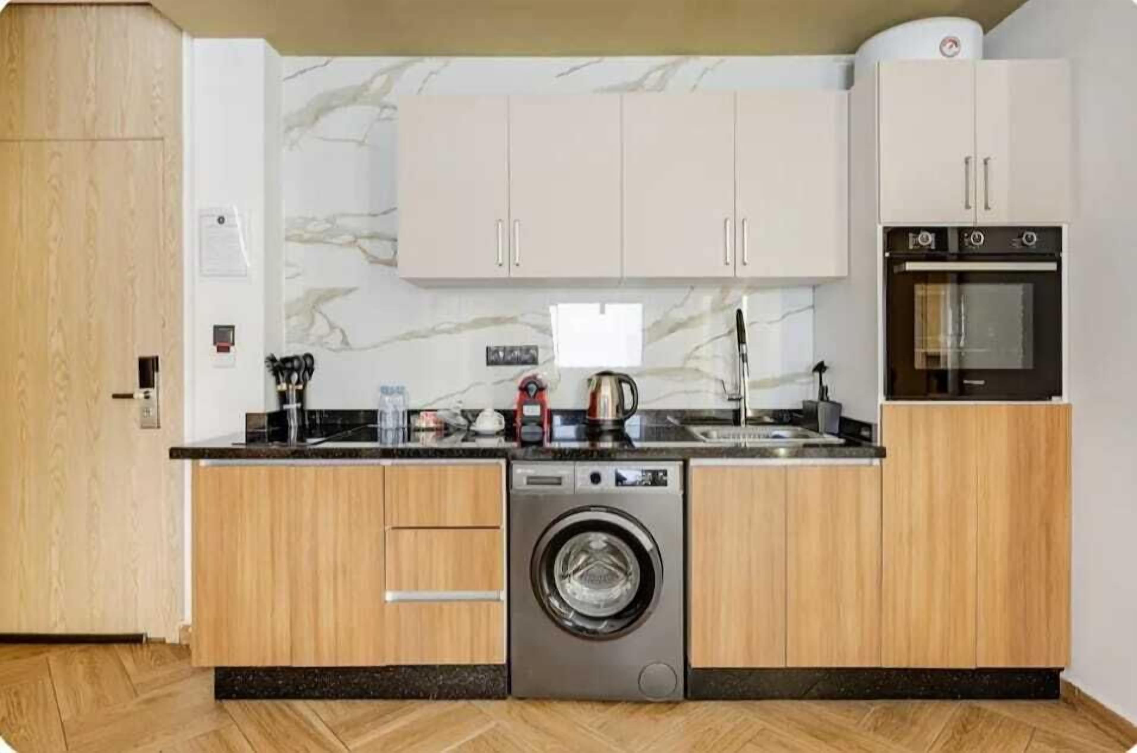 A compact kitchen with wooden cabinets, a built-in washing machine, and a microwave.