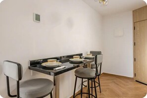A small kitchen with a black countertop, two bar stools, and a wooden door.