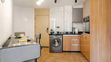 Cocina compacta con lavadora, armarios de madera y comedor con mesa para dos.