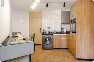 Cocina compacta con lavadora, armarios de madera y comedor con mesa para dos.