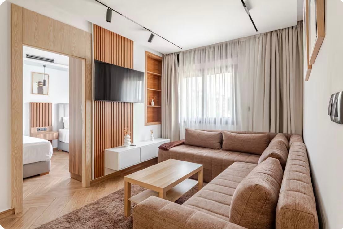 Een moderne woonkamer met een bank, een salontafel en een aan de muur bevestigde televisie.