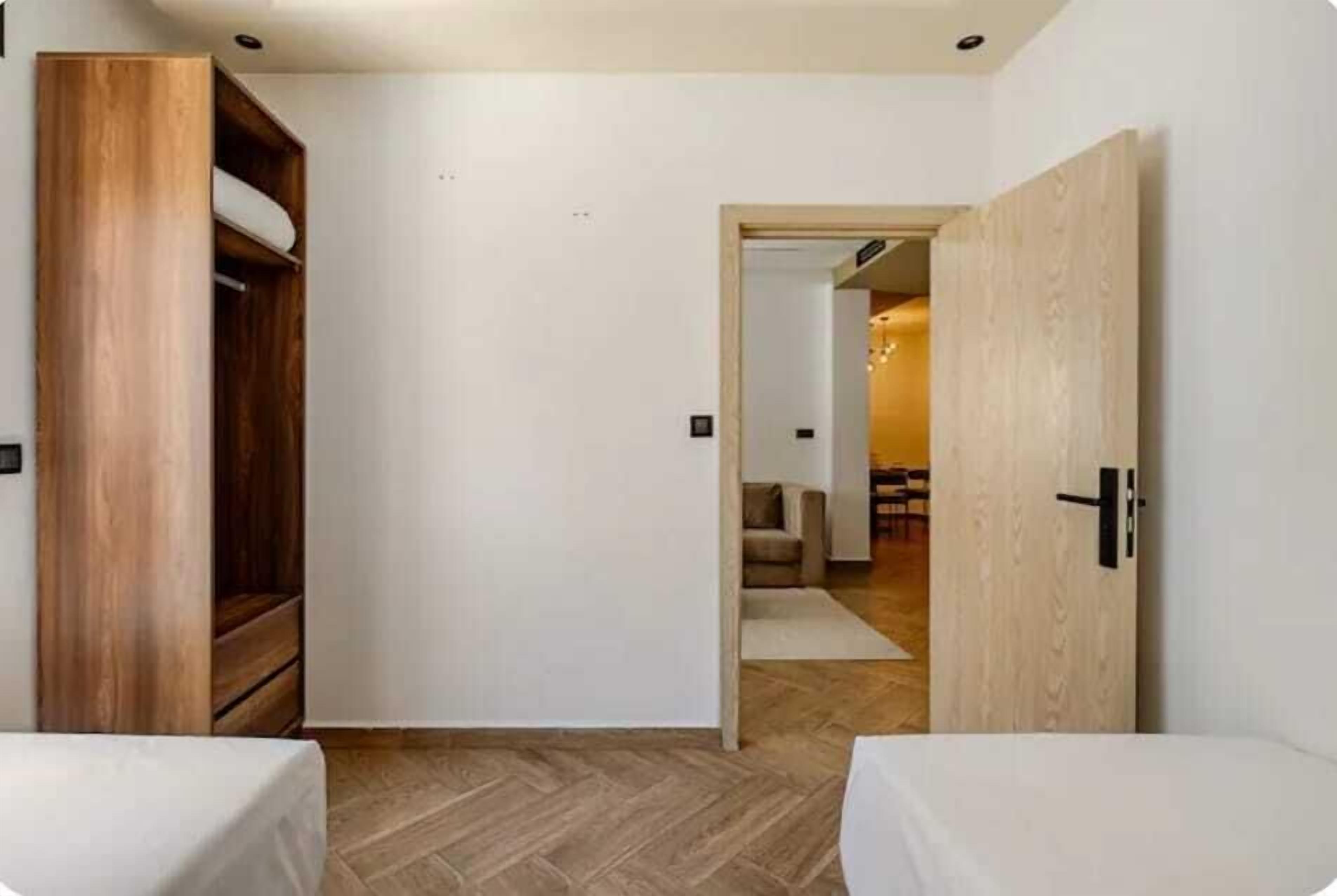 A bedroom with a wooden wardrobe, a bed, and a door leading to another room.