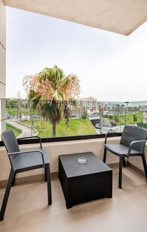 Un balcon avec deux chaises, une petite table et une vue sur un palmier et le paysage urbain.