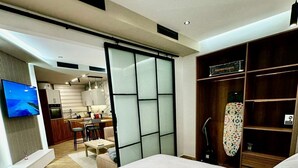 Une chambre moderne dotée d’un grand lit, d’un téléviseur fixé au mur, d’une kitchenette et d’une porte-fenêtre coulissante donnant sur un coin repas.
