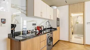A compact kitchen with a washing machine, wooden cabinets, and a marble backsplash.