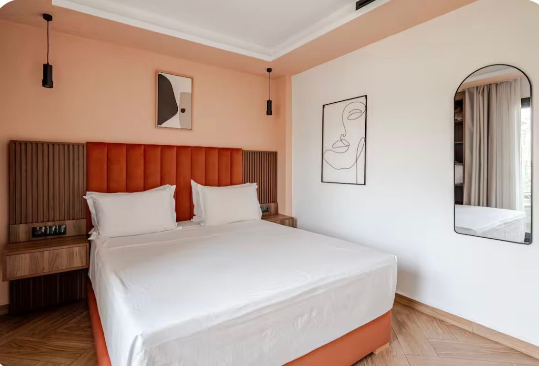 Une chambre d’hôtel avec un grand lit, une table de chevet, une commode, un miroir fixé au mur et un mur orné de deux œuvres d’art encadrées.