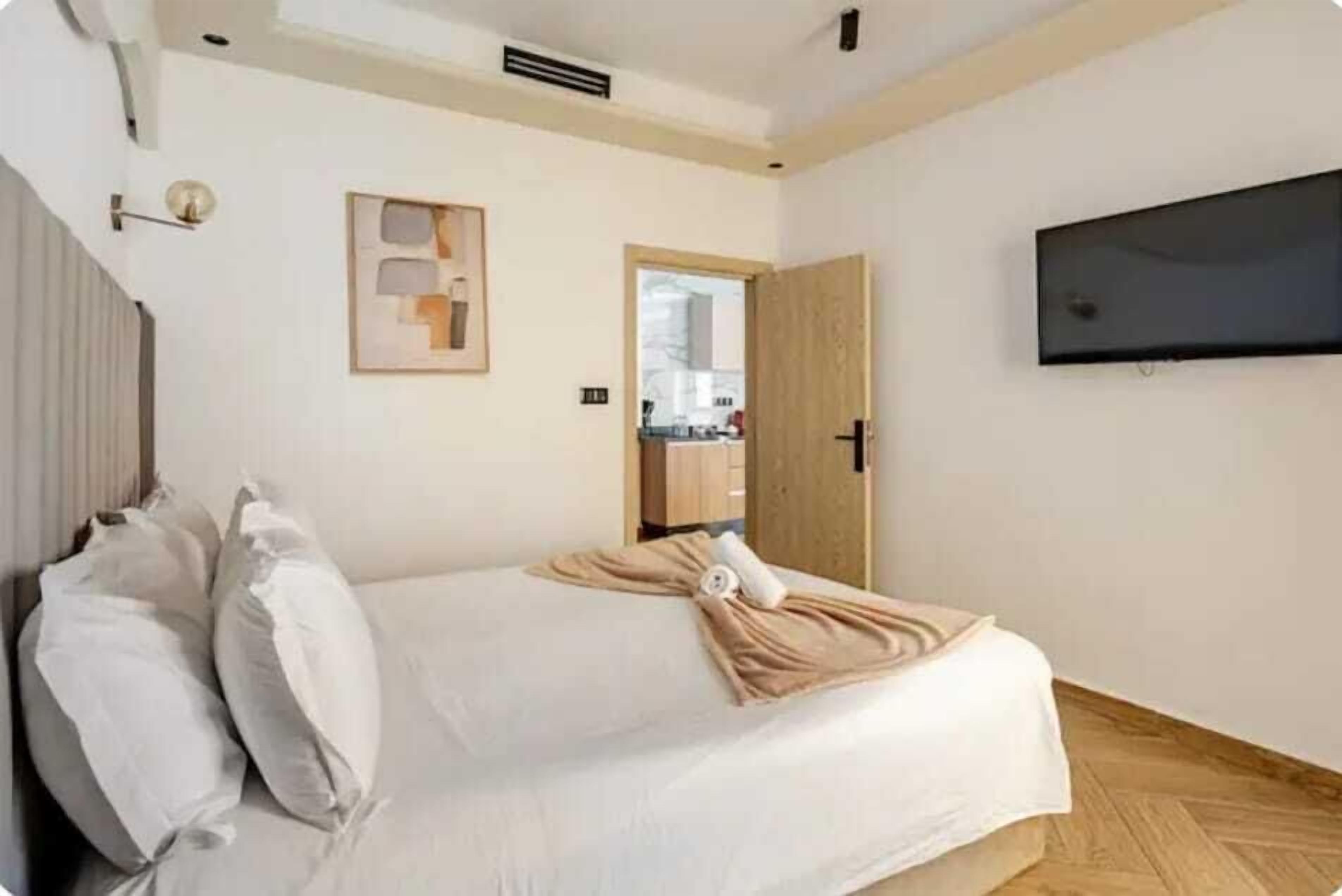 Una camera da letto con un letto, cuscini, una TV fissata al muro e una porta in legno.