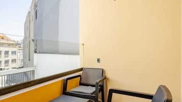 A balcony with a table and two chairs, a yellow wall, and a view of buildings.