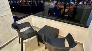 Un balcon avec deux chaises et une petite table, d’où l’on peut admirer la vue sur la ville au crépuscule.