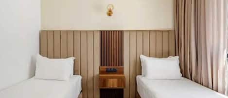 A hotel room with two single beds, a wooden headboard, a nightstand, and a wall-mounted light fixture.