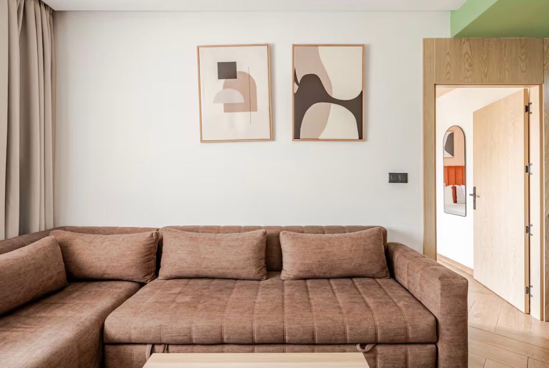 Una sala moderna con un sofá modular, dos obras de arte abstracto y una puerta de madera.