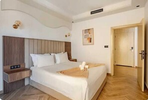 A hotel room with a large bed, a wooden headboard, a bedside table, and a wall-mounted light fixture.