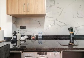 Et køkken med marmorbeklædt væg, indbygget ovn, kaffemaskine og vanddispenser.