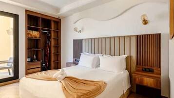 A hotel room with a bed, a wooden wardrobe, a bedside table, and a wall-mounted light fixture.