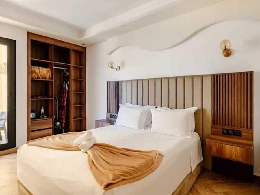 A hotel room with a bed, a wooden wardrobe, a bedside table, and a wall-mounted light fixture.