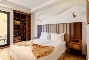 Una habitación de hotel con una cama, un armario de madera, una mesita de noche y una lámpara fijada a la pared.