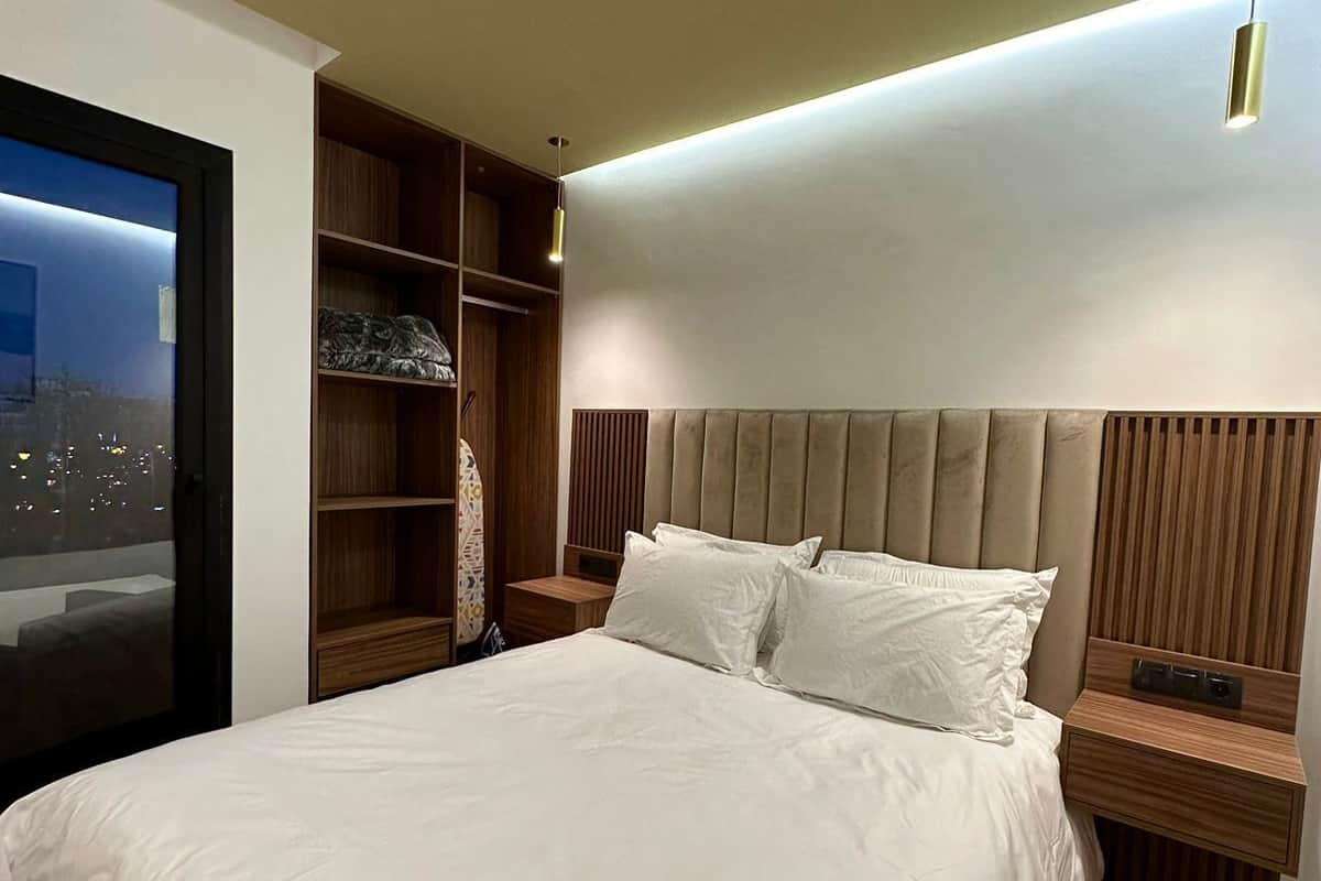 A modern hotel room with a large bed, wooden headboard, and built-in shelving.