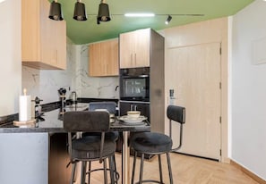 A compact kitchen with a marble backsplash, wooden cabinets, a black countertop, and bar stools.