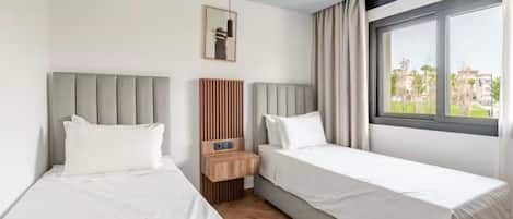 A hotel room with two beds, a wooden nightstand, a framed picture, and a window with curtains.