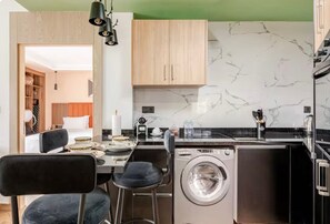 A compact kitchen with a washing machine, wooden cabinets, and a marble backsplash.