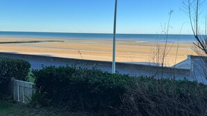 A beach with a clear view of the ocean, a concrete barrier, and some greenery in the foreground.