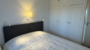 A bedroom with a bed, a nightstand, a wall-mounted lamp, and a wardrobe.