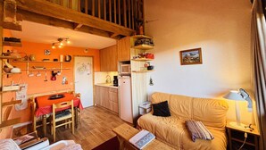 Un salon chaleureux avec un escalier en bois, un coin repas avec une table rouge et une cuisine équipée d’un four à micro-ondes et de bibliothèques.