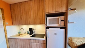 Une cuisine compacte avec des meubles en bois, un évier blanc, une machine à café, un four à micro-ondes et un réfrigérateur.