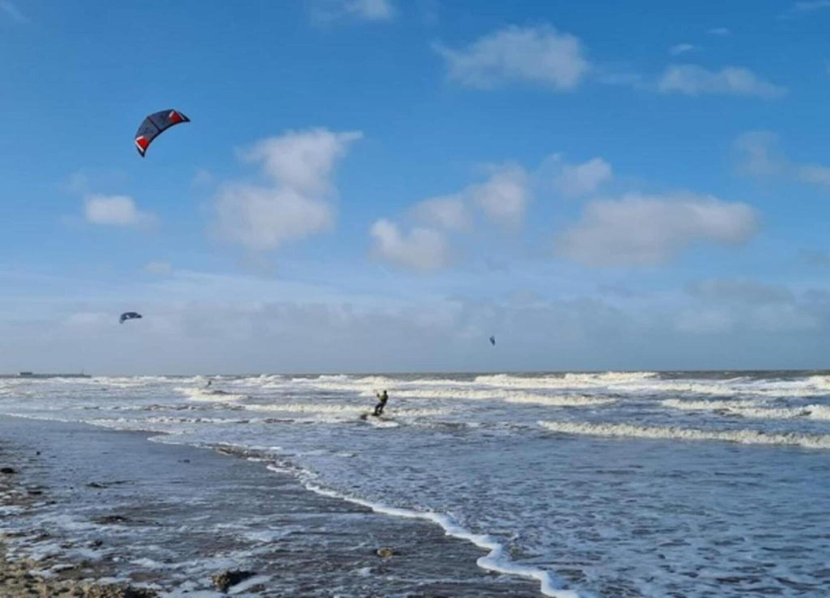 A beach with waves and a person kite surfing.