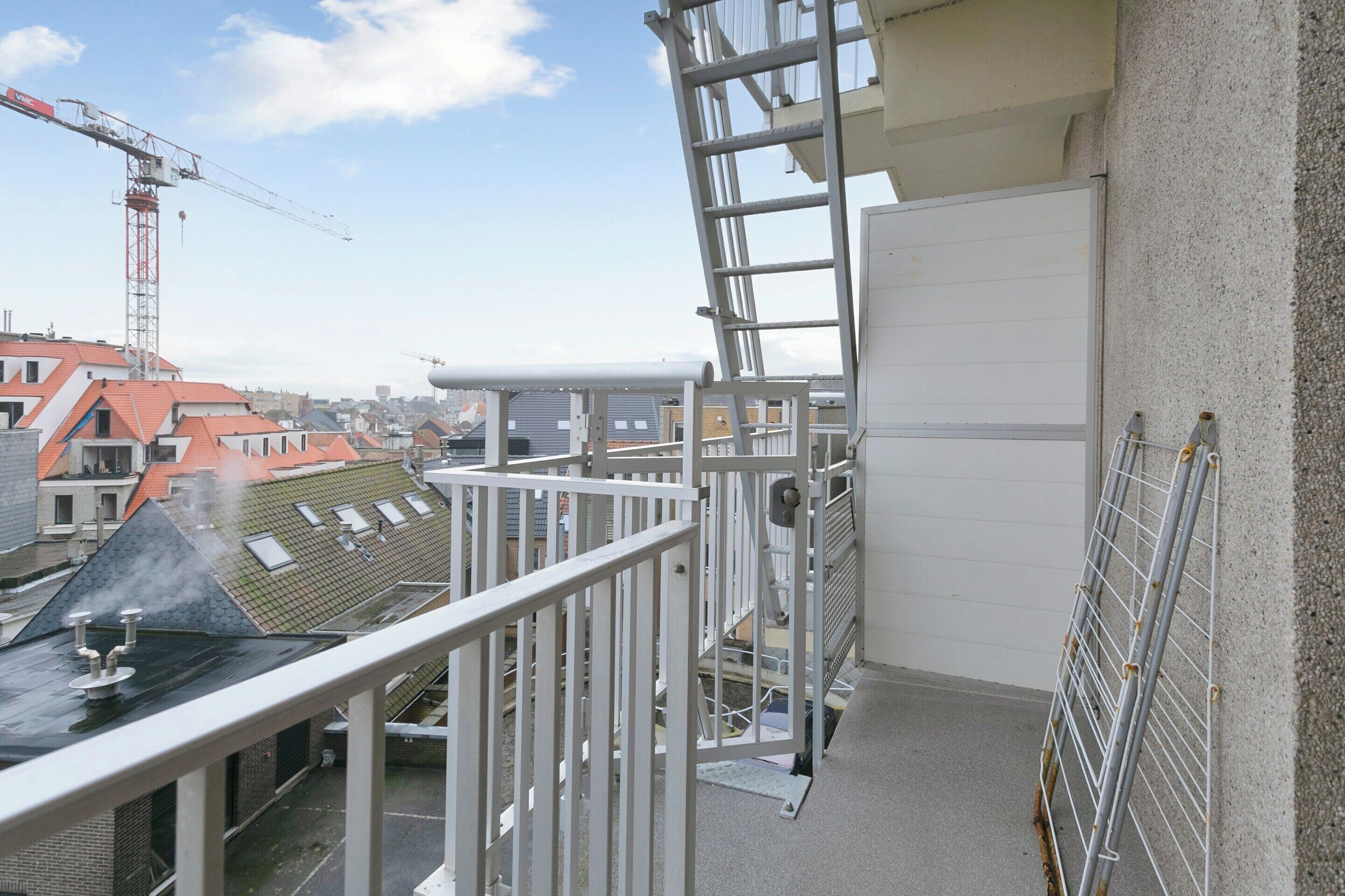 Une terrasse sur le toit, dotée d’une rambarde en métal, d’une échelle et offrant une vue sur les bâtiments environnants.