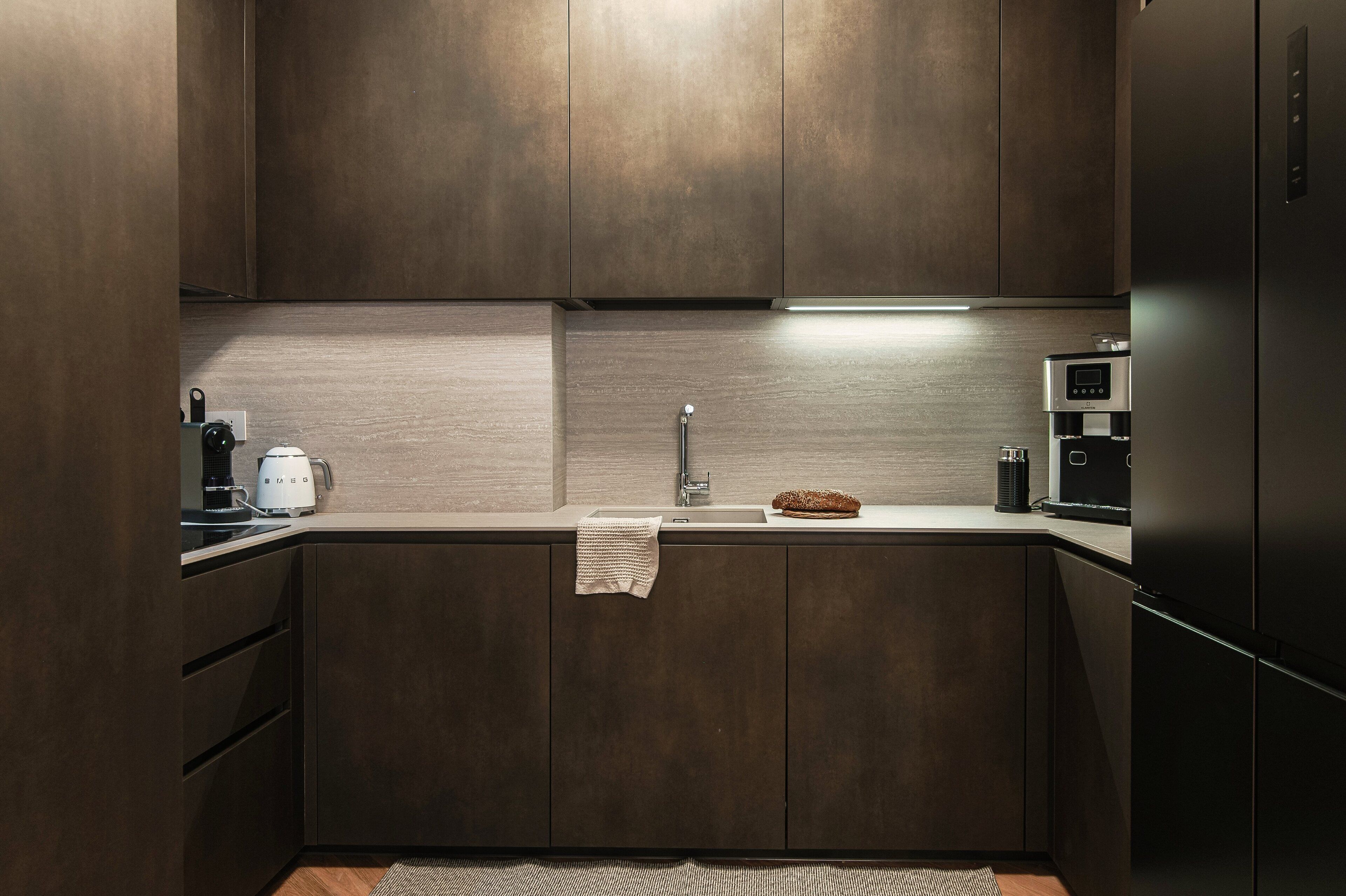 A modern kitchen with dark wood cabinets, a stainless steel refrigerator, a coffee maker, and a microwave.