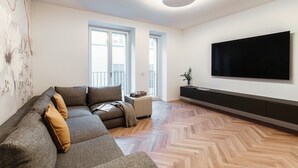 Ein modernes Wohnzimmer mit einem Ecksofa, einem flachbildfernseher an der Wand und einem Holzboden mit Zickzackmuster.