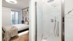 Ein modernes Badezimmer mit Duschkabine aus Glas und ein separates Schlafzimmer mit Bett und Balkonblick.