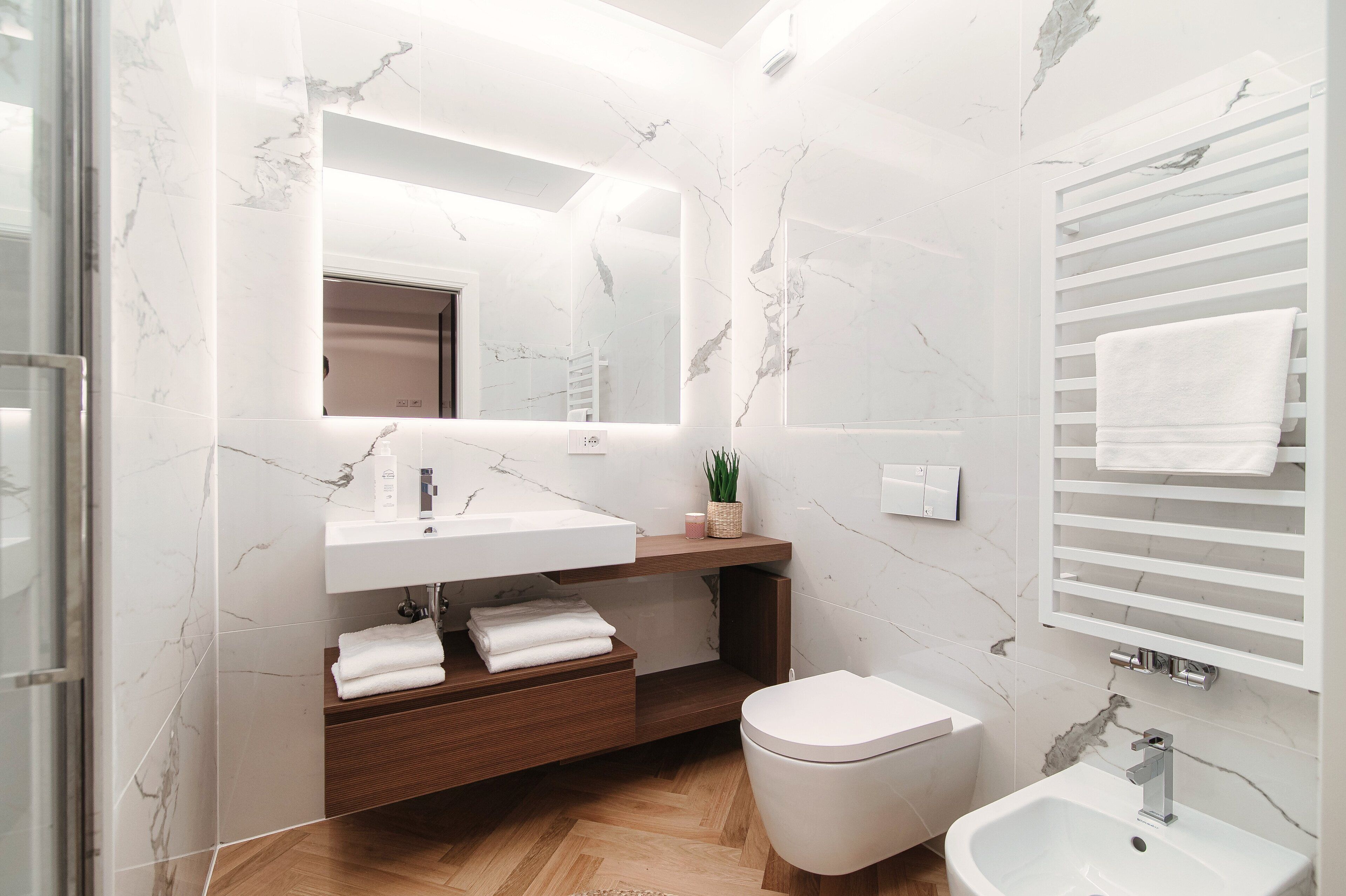 A modern bathroom with a marble backsplash, a wooden vanity, a white toilet, and a bidet.
